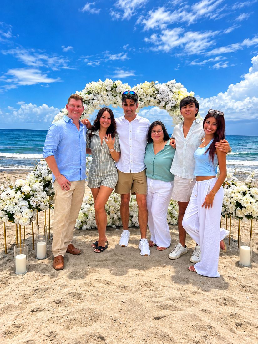 Ryan and Wendy with family under the floral heart on the beach on engagement day