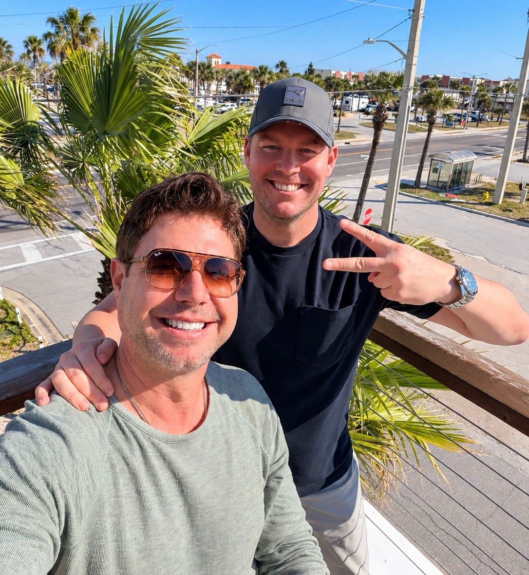 Ryan and a friend smiling on a balcony above a palm-lined street